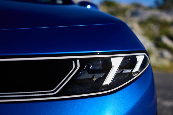 لقطة مقربة لعجلة سوداء وفضية في BMW i3 الأزرق أمام طلاء أزرق وأسفلت.