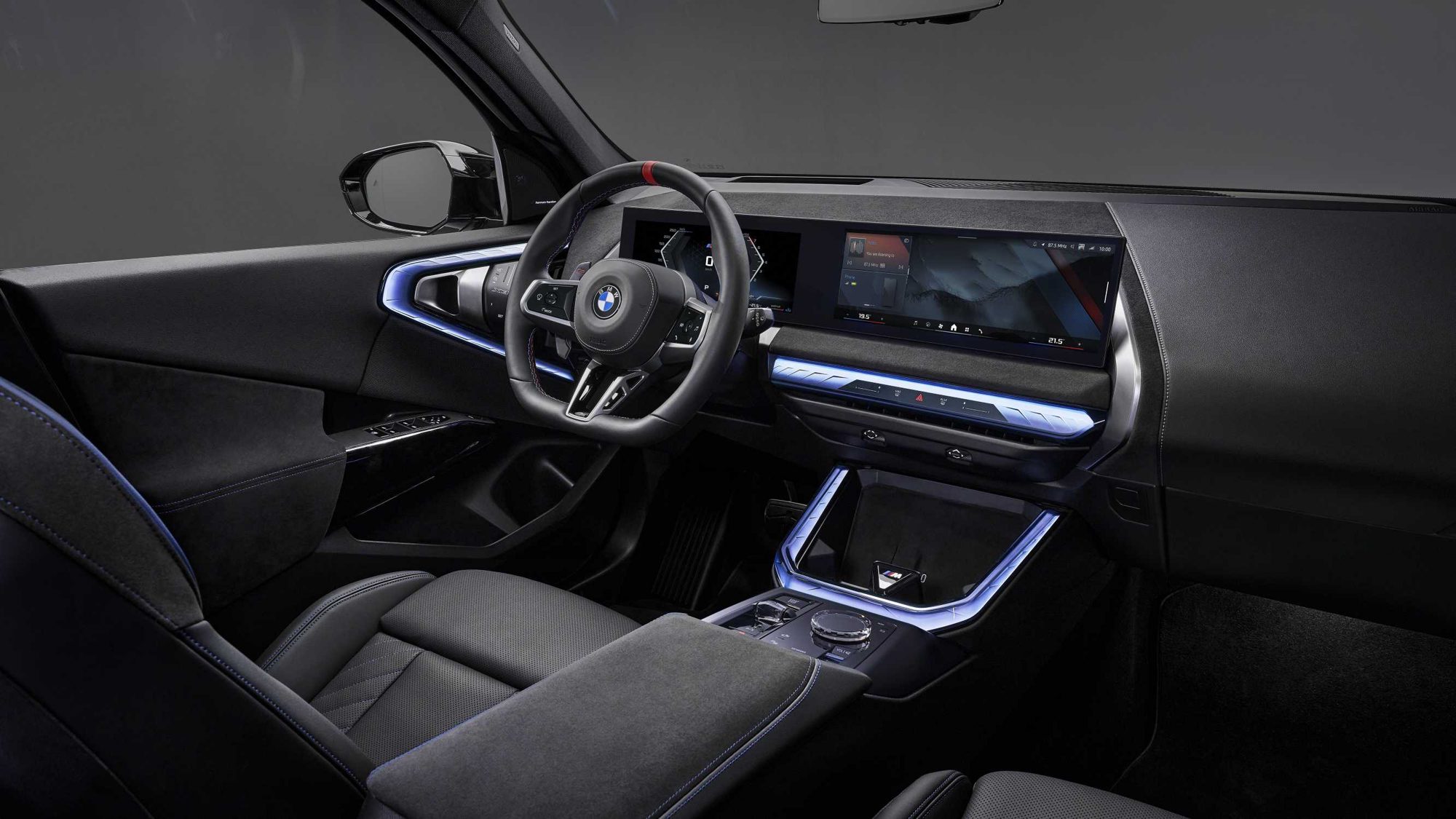 موضع السائق في BMW X3 M50 xDrive مع عجلة قيادة وشاشة عريضة ولمسات إضاءة زرقاء.