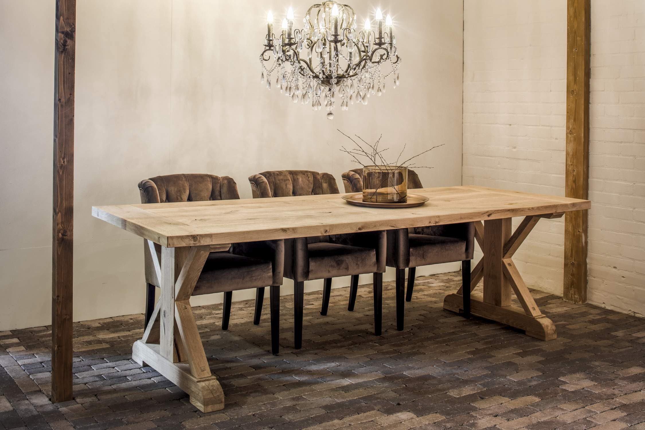 Langer Esstisch aus hellem Holz mit X-Gestell, braunen Polsterstühlen und Kristallleuchter.
